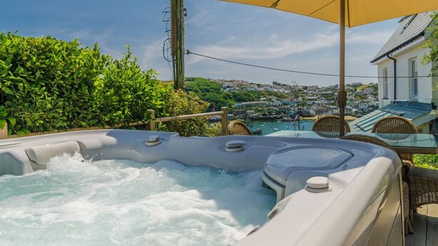 A hot tub with a view of a town, surrounded by greenery and a large umbrella. - Entire Victorian Schoolhouse With hot tub and Harbour Views (Fowey)
