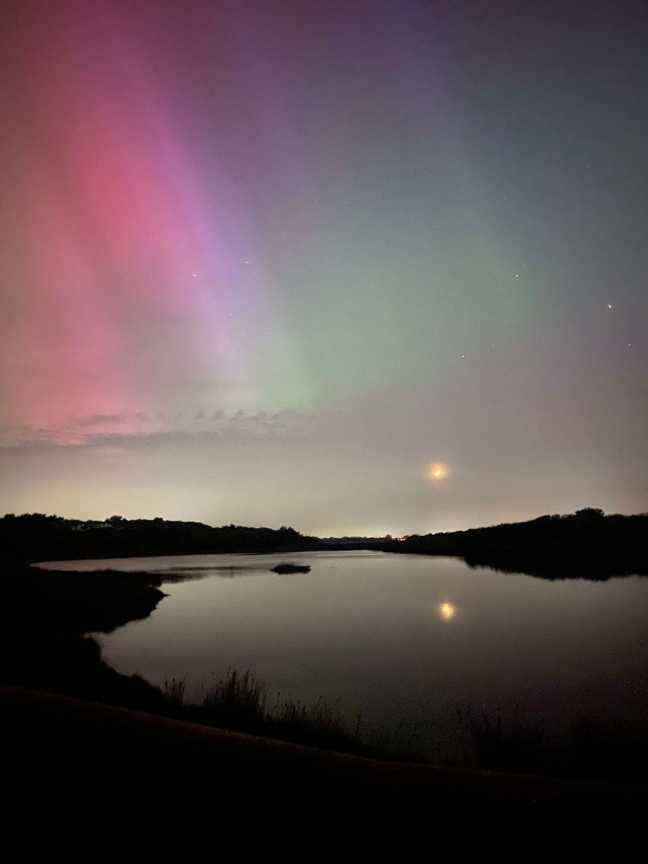 A nighttime landscape with a calm body of water reflecting the sky.