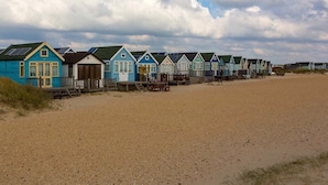 A row of beach huts with a sandy beach in the foreground. - Stargaze From a Beach hut on the Mudeford Sandbank (Bournemouth)