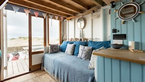 A cozy room with a bed, a wooden bench, a mirror, and a view of the beach. - Stargaze From a Beach hut on the Mudeford Sandbank (Bournemouth)