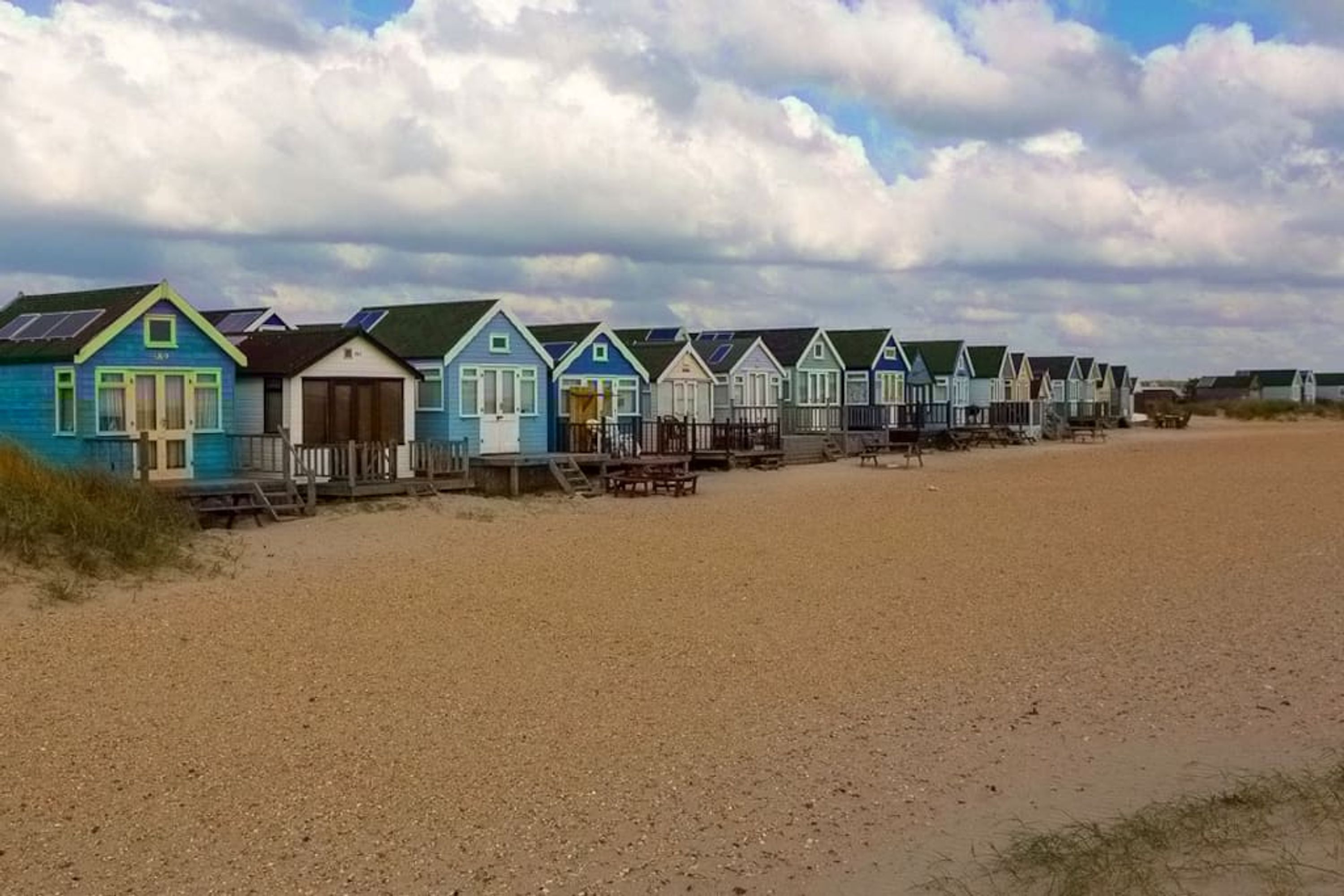 A row of beach houses with solar panels, wooden decks, and a sandy beach.