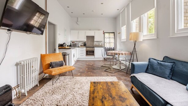 A modern living room with a sofa, a coffee table, and a TV mounted on the wall. - Converted Flat in Amazing Converted Schoolhouse Near Fowey Harbour (Fowey)
