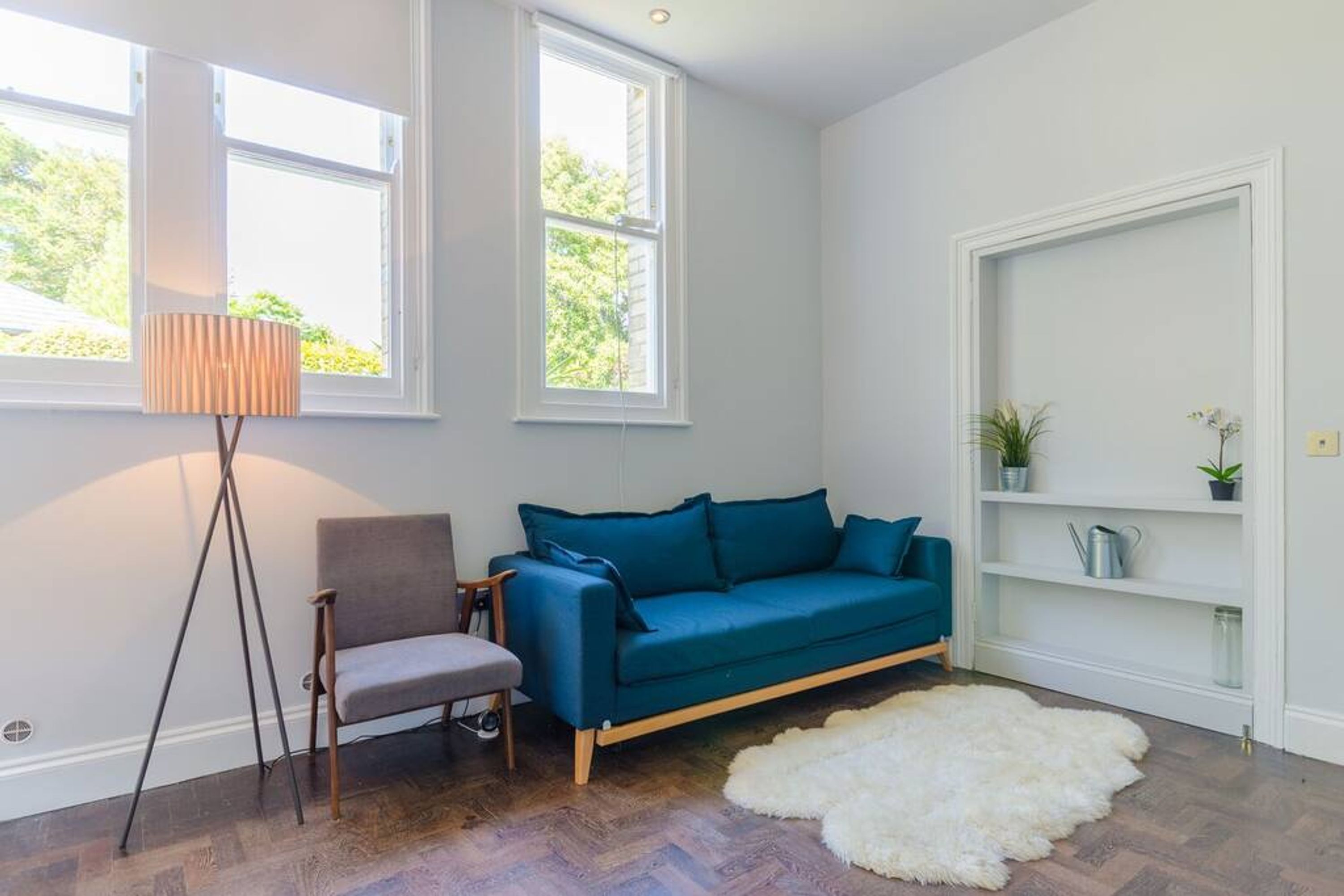 Una habitación con un sofá azul, una silla, un tapete blanco y una lámpara de pie.
