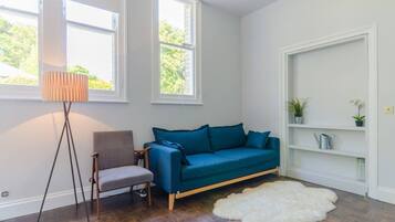 Una habitación con un sofá azul, una silla, un tapete blanco y una lámpara de pie.