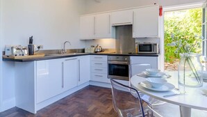 Una cocina moderna con armarios blancos, una campana extractora de acero inoxidable, microondas y un comedor con mesa y sillas.