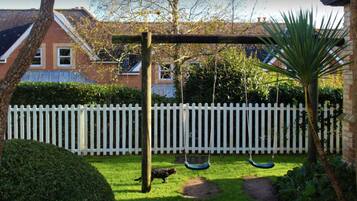 A backyard with a swing set, a white picket fence, and a house in the background.