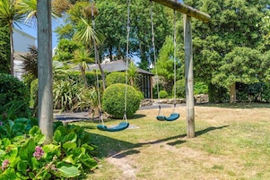 A garden with a swing set, a stone wall, and a building in the background.