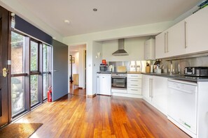 A modern kitchen with white cabinets, stainless steel appliances, and a wooden floor. - Charming Summerhouse in Fowey Town Center (Fowey)