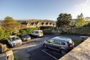 A parking area with cars, a stone wall, and a row of houses in the background.