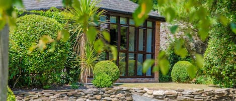 A building with a stone wall, a paved driveway, and well-maintained bushes.