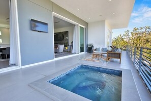 Una piscina interior moderna con borde de azulejos, un televisor de pantalla plana en la pared y un balcón con barandilla que da a un paisaje tropical.