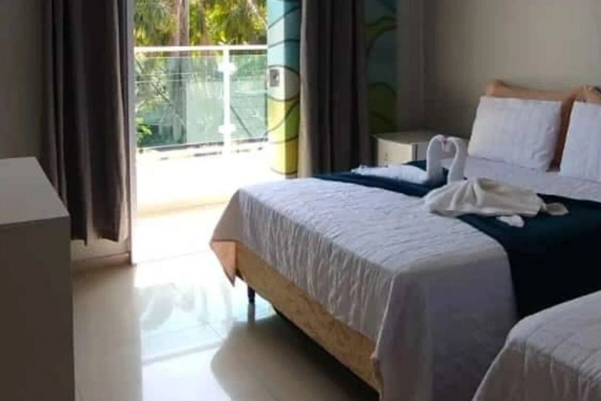 A hotel room with a bed, a bedside table, and a view of the outside.