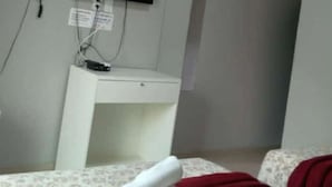 Ein Zimmer mit einem Bett, einem kleinen Schreibtisch und einem an der Wand montierten Fernseher.