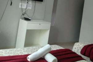 Una habitación con una cama, un escritorio pequeño y un televisor fijado a la pared.