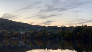 A calm lake with reflections of trees and houses, surrounded by hills and a clear sky. - Apartment for 2 People (25 m²) in Kreuzau (Kreuzau)