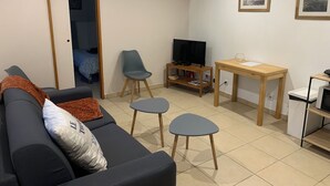 Uma sala de estar com sofá, televisão sobre um suporte, uma mesinha e uma cadeira.