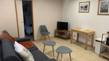 Un salon avec un canapé, un téléviseur posé sur un meuble, une petite table et une chaise.