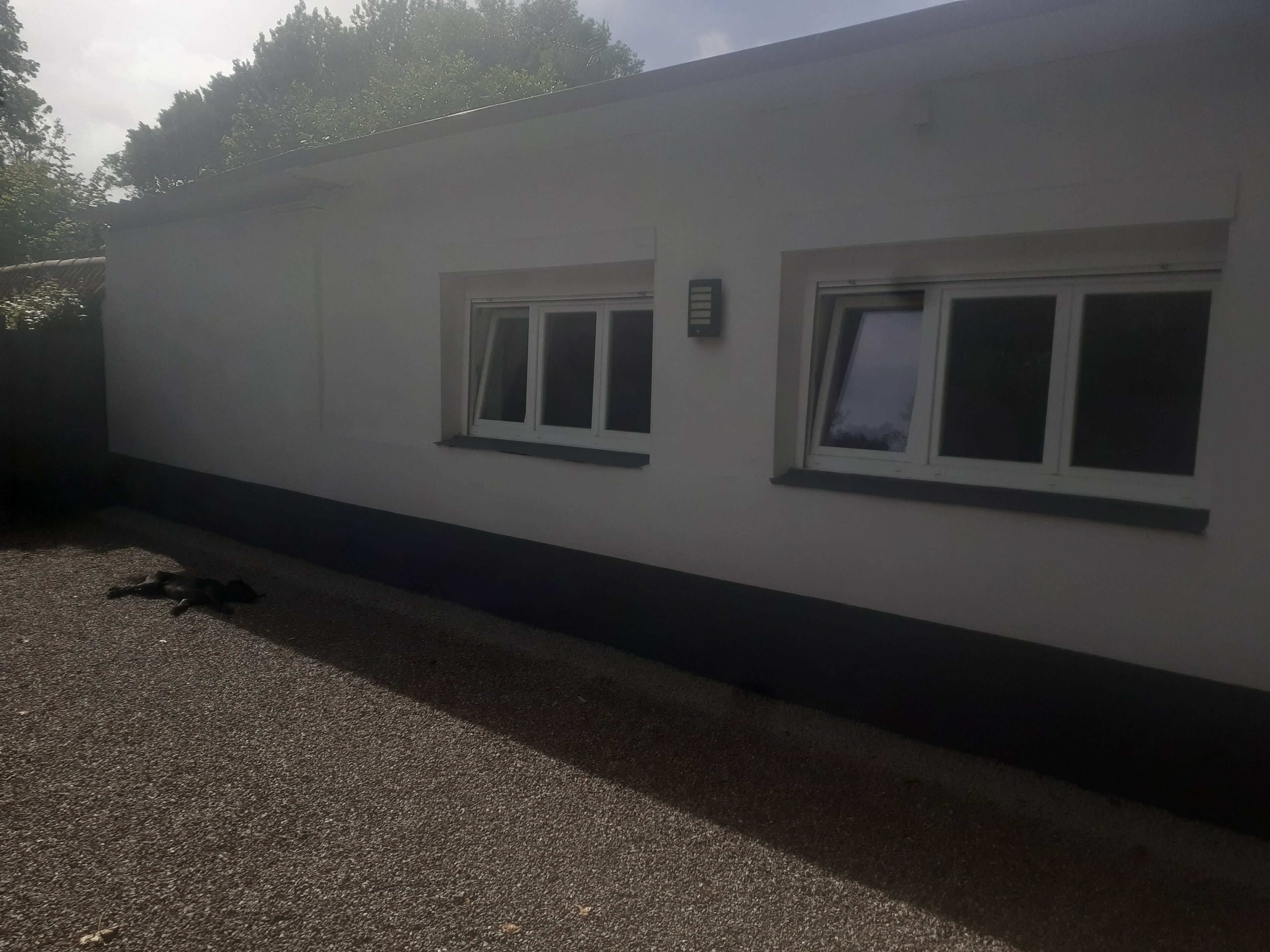 A building with two windows, a door, and a gravel driveway.