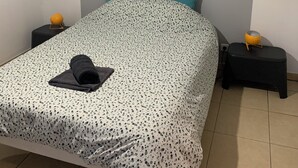 Quarto com cama, cabeceira, quadro na parede, duas mesas de cabeceira com luminárias e um cobertor na cama.