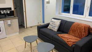 Uma sala de estar com sofá, duas mesinhas, máquina de lavar e janela com vista.