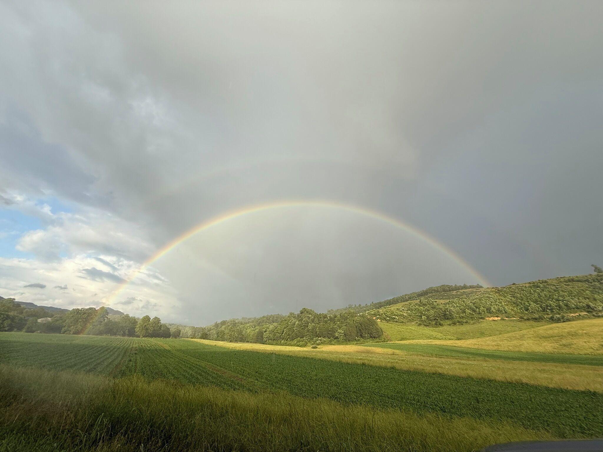 Maisema, jossa näkyy sateenkaari pellon yllä.