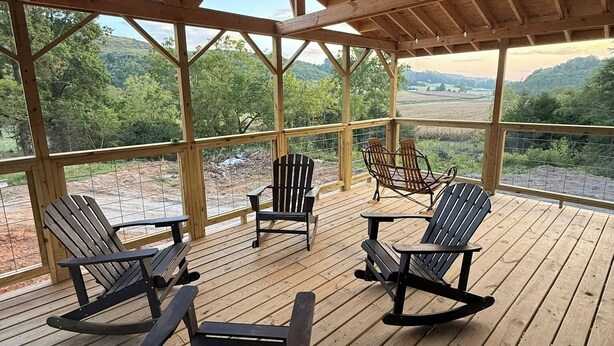 A covered deck with wooden furniture and a view of the surrounding landscape. - Scenic Farm Loft in Amish Country w/ Epic Views (Jonesville)