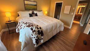 A bedroom with a large bed, two bedside lamps, a painting on the wall, and a door leading to a bathroom. - Scenic Farm Loft in Amish Country w/ Epic Views (Jonesville)