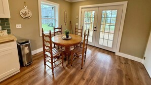 A dining area with a round table, wooden chairs, a trash can, and a window with a view of a backyard. - Scenic Farm Loft in Amish Country w/ Epic Views (Jonesville)