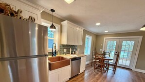 A kitchen with a stainless steel refrigerator, a wooden countertop, white cabinets, and a dining area with wooden chairs. - Scenic Farm Loft in Amish Country w/ Epic Views (Jonesville)