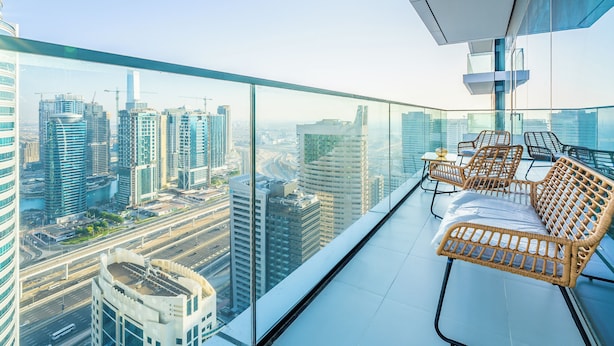 Un edificio alto con un balcone in vetro, mobili in vimini e vista sulla città.
