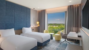 Ein Hotelzimmer mit zwei Betten, einem Schreibtisch, einem Stuhl, einem Fernseher und einem großen Fenster mit Blick.