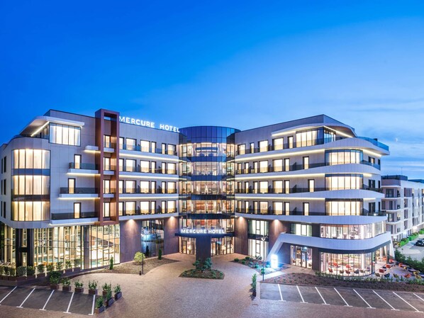 A modern hotel with a curved facade, multiple balconies, and a well-lit entrance. - Mercure Oradea (Oradea)