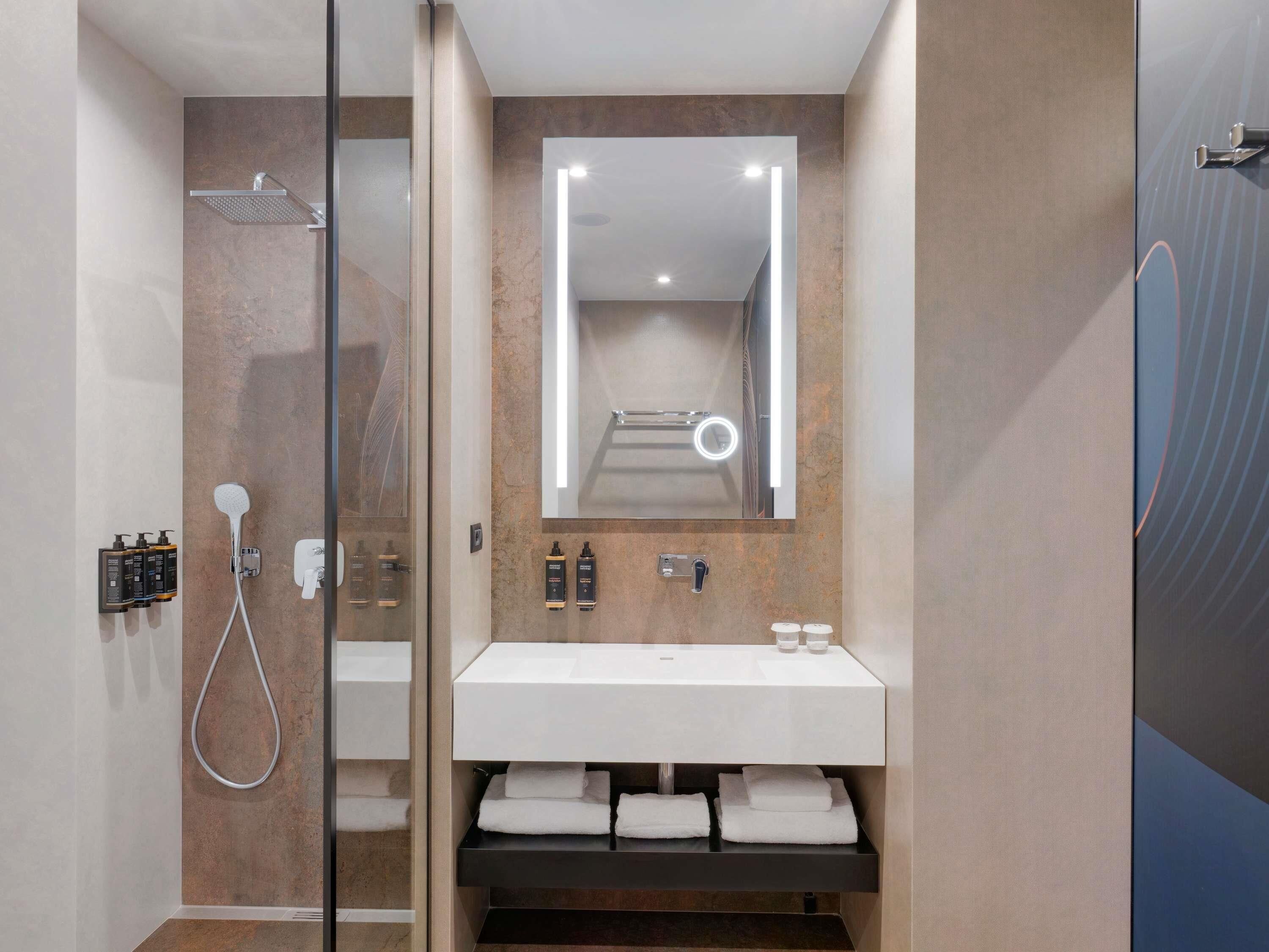 A modern bathroom with a glass-enclosed shower, a white sink, and a mirror with integrated lighting.