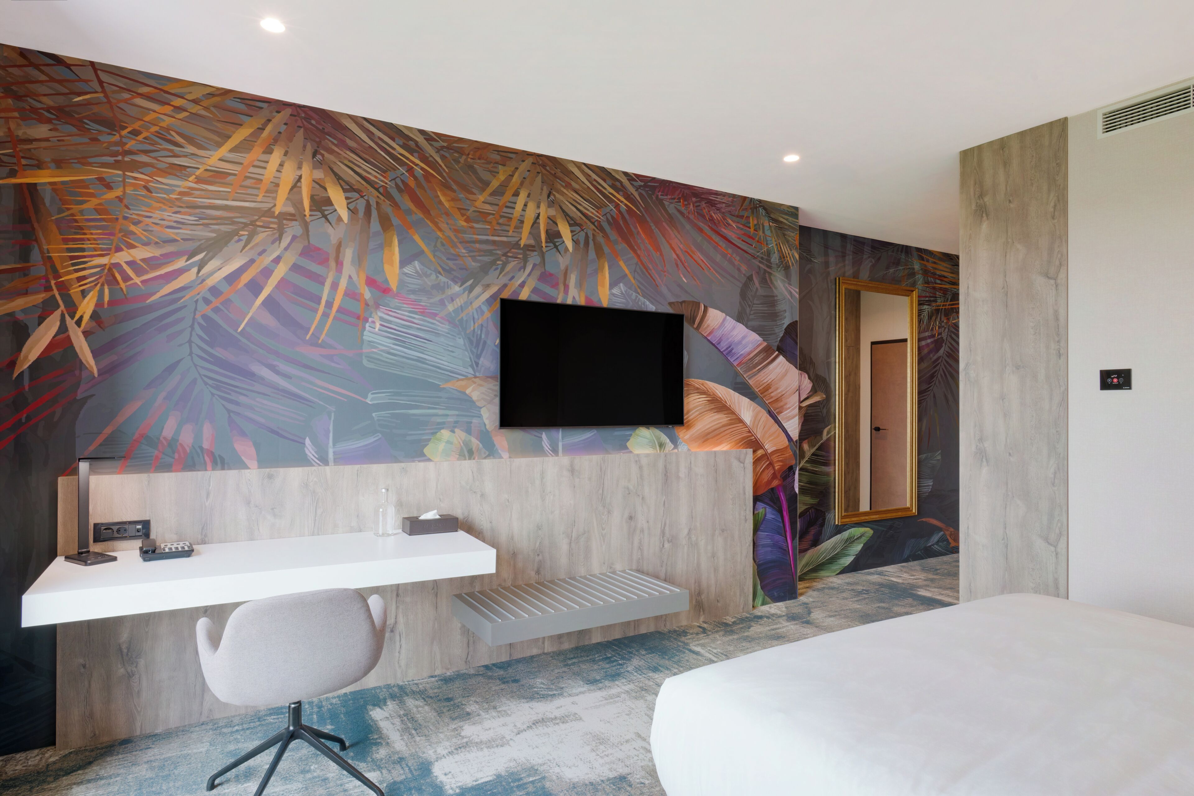 A hotel room with a desk, chair, bed, and a large wall mural.