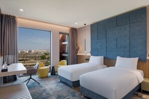 A hotel room with two beds, a desk, a chair, and a large window offering a city view. - Mercure Oradea  (Oradea)