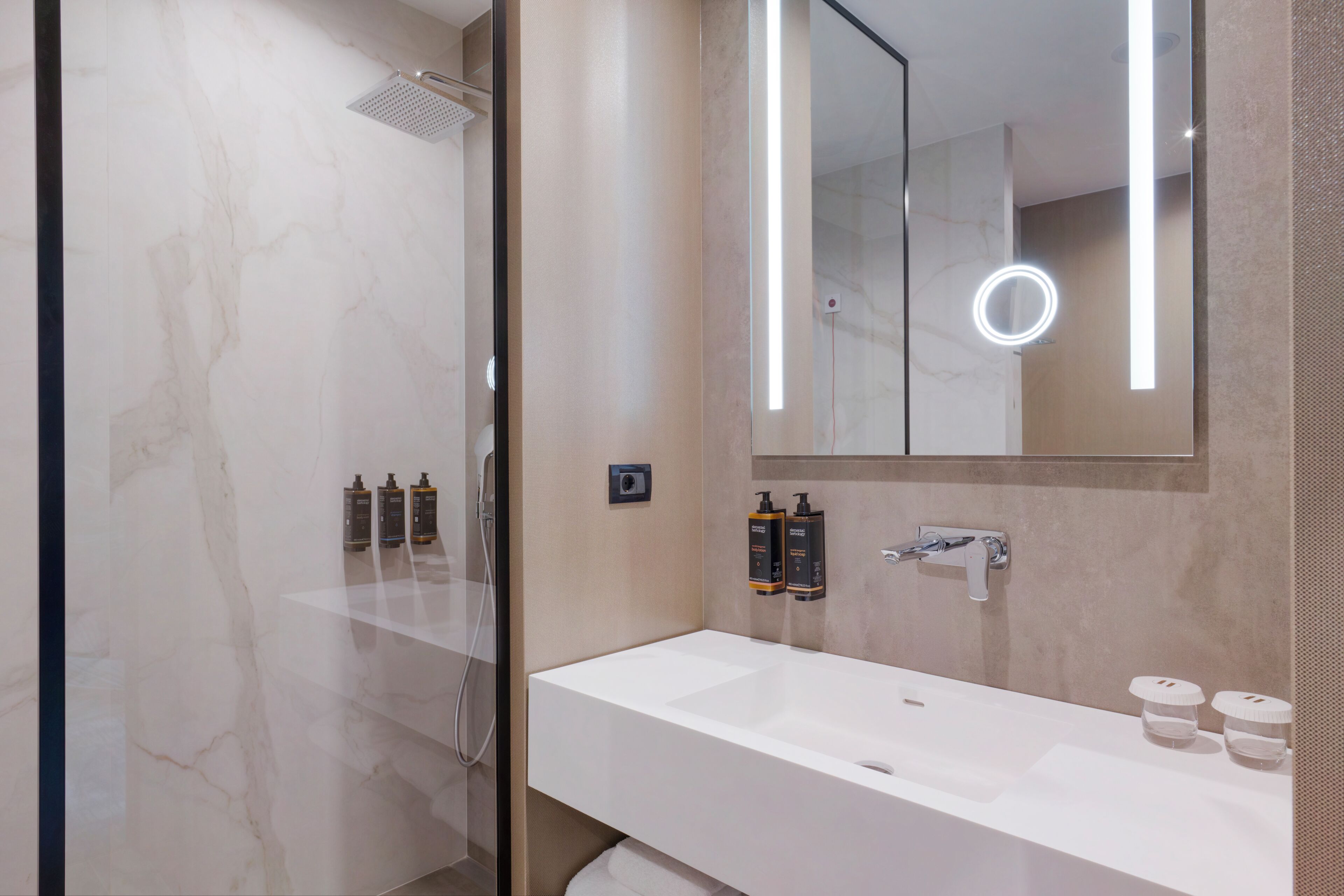 A modern bathroom with a glass shower enclosure, a white sink, and a large mirror with integrated lighting.