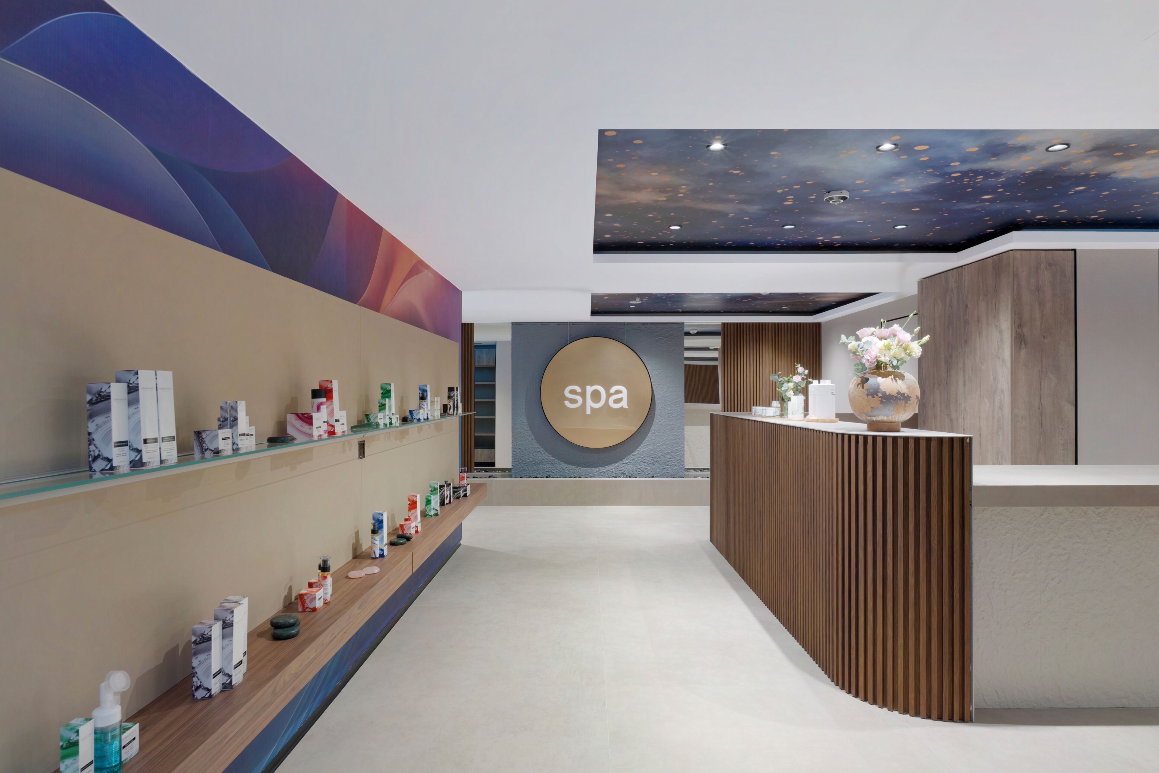 A spa reception area with a modern design, including a reception desk, a wall-mounted spa sign, and a variety of spa products displayed on shelves.