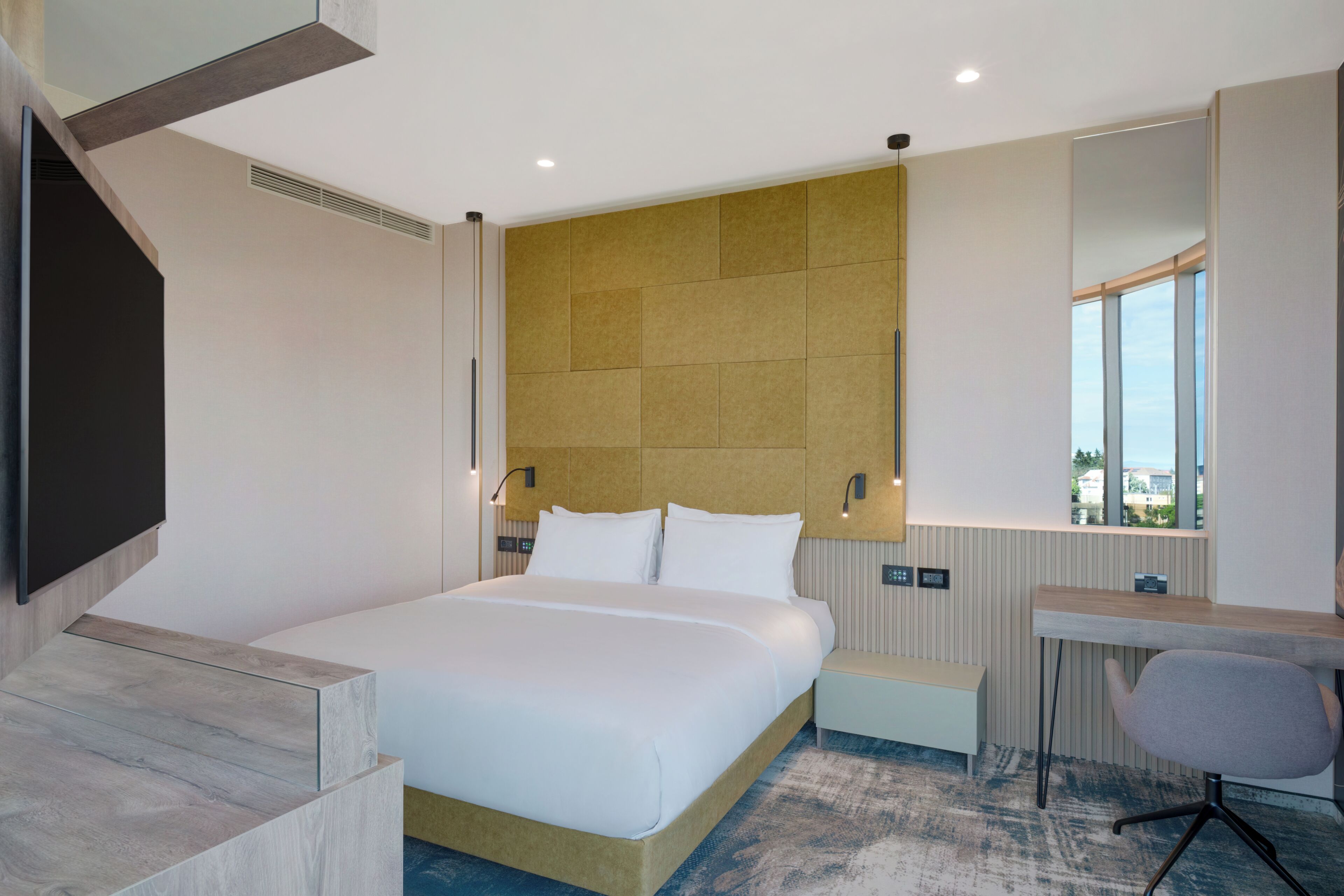 Ein modernes Hotelzimmer mit einem großen Bett, einem Schreibtisch und einem Fernseher.