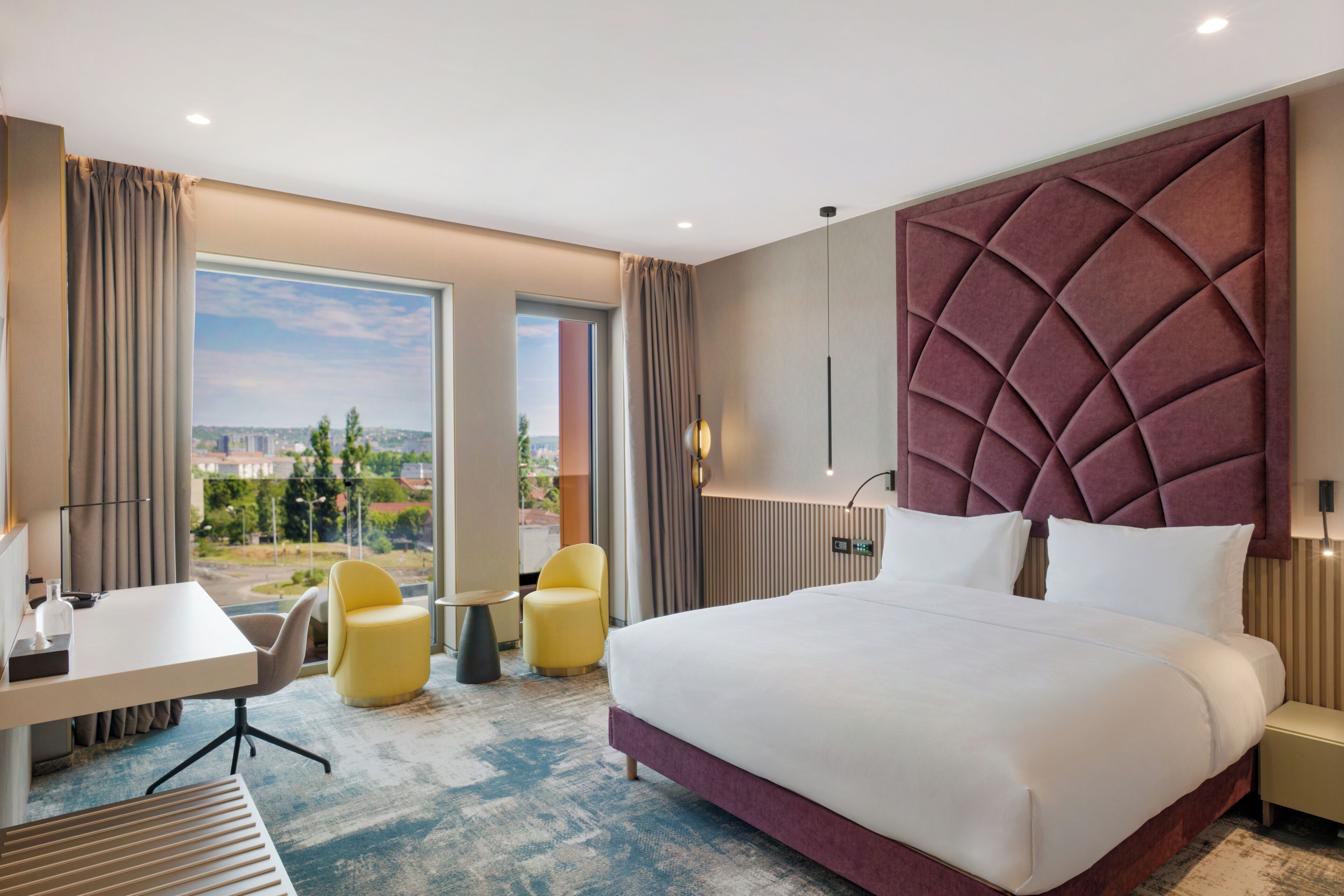Habitación de hotel con una cama grande, un escritorio, dos sillas y vistas a la ciudad.