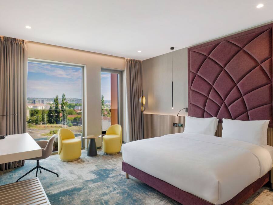 Habitación de hotel con una cama grande, un escritorio, dos sillas y vistas a la ciudad.
