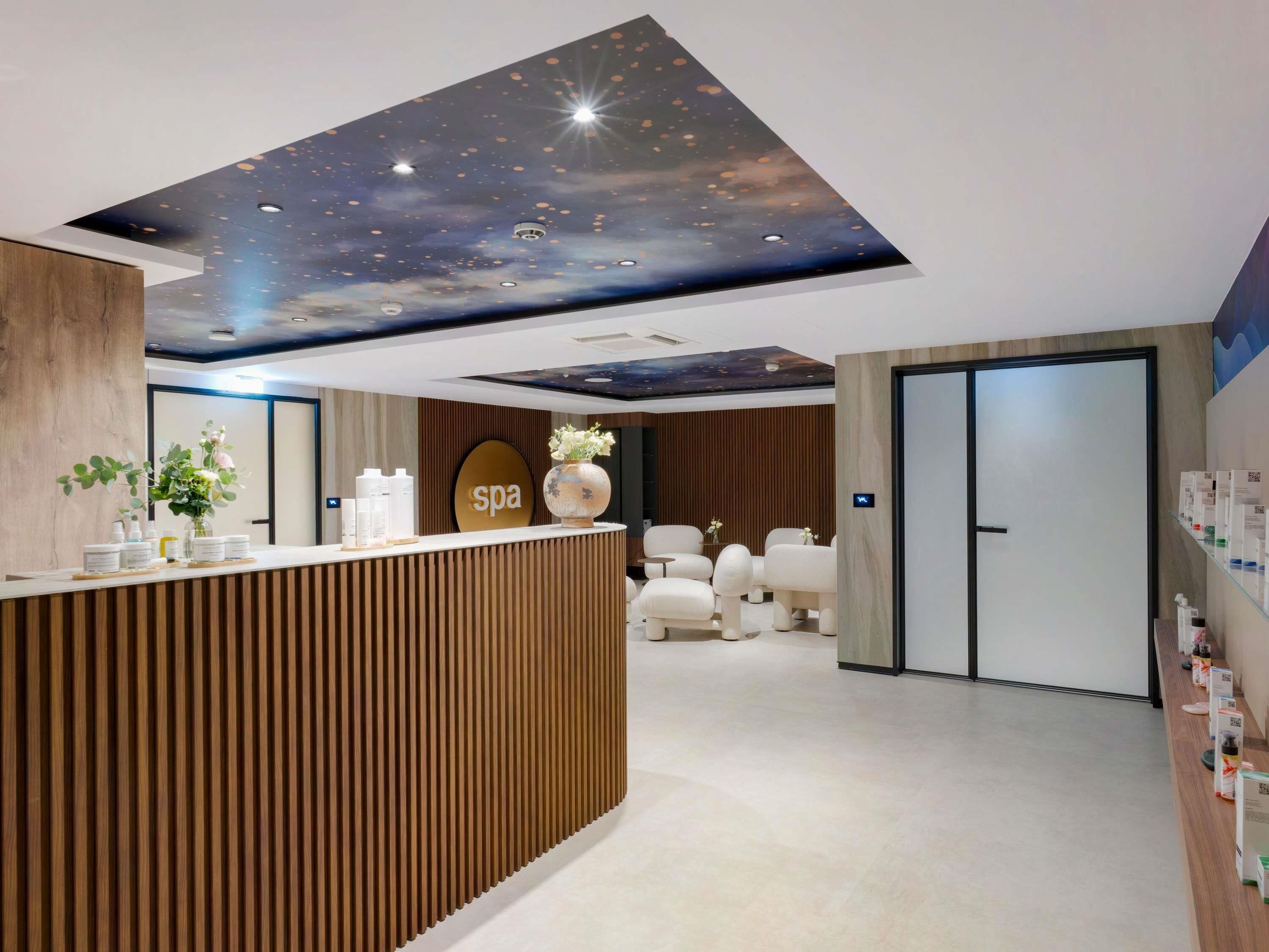 Zona de recepción de un spa, con un mostrador de madera, un cartel que dice 'spa' y un techo decorado con un diseño de cielo estrellado.