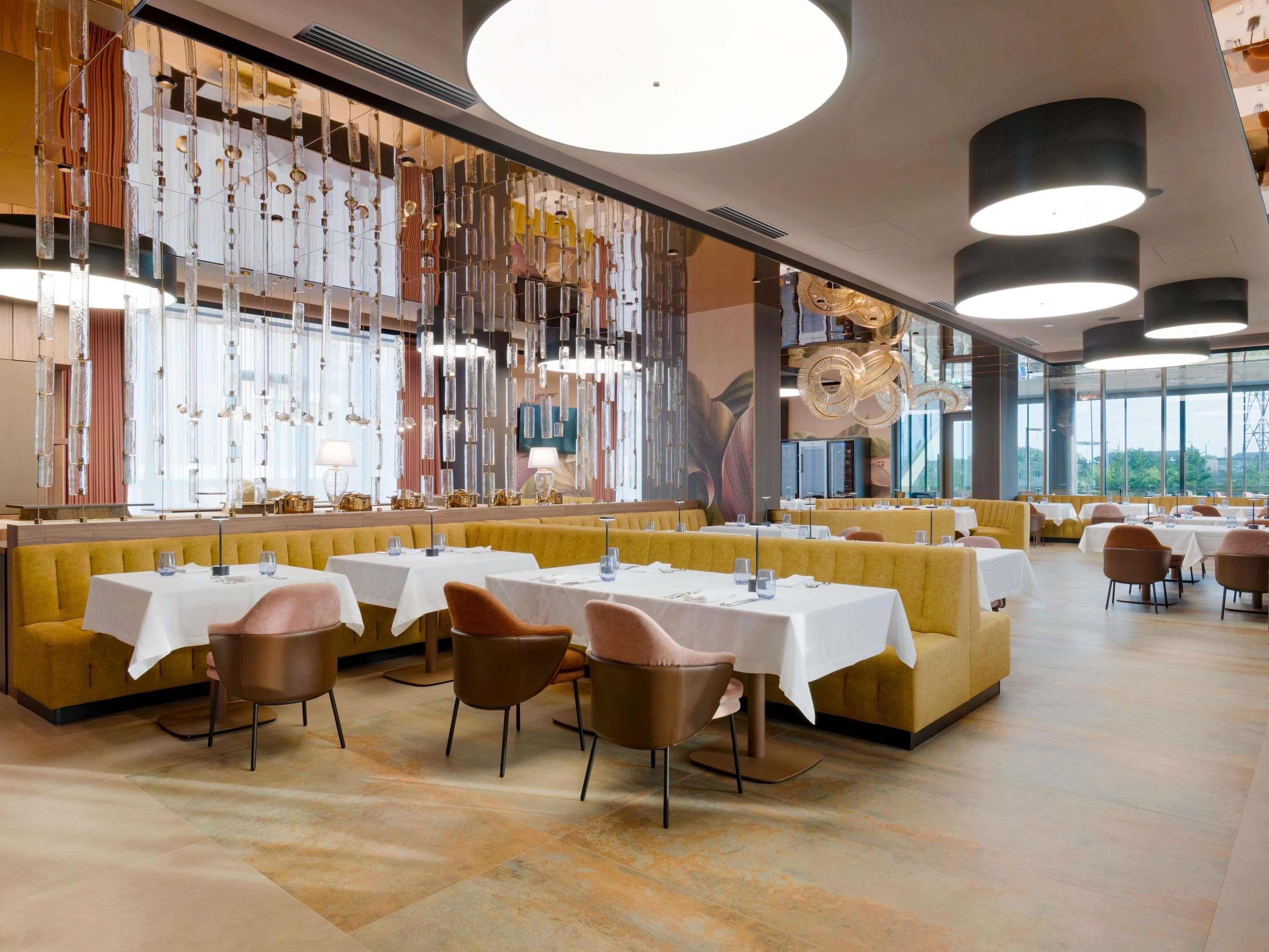 A restaurant interior with booths, round tables, and hanging light fixtures.