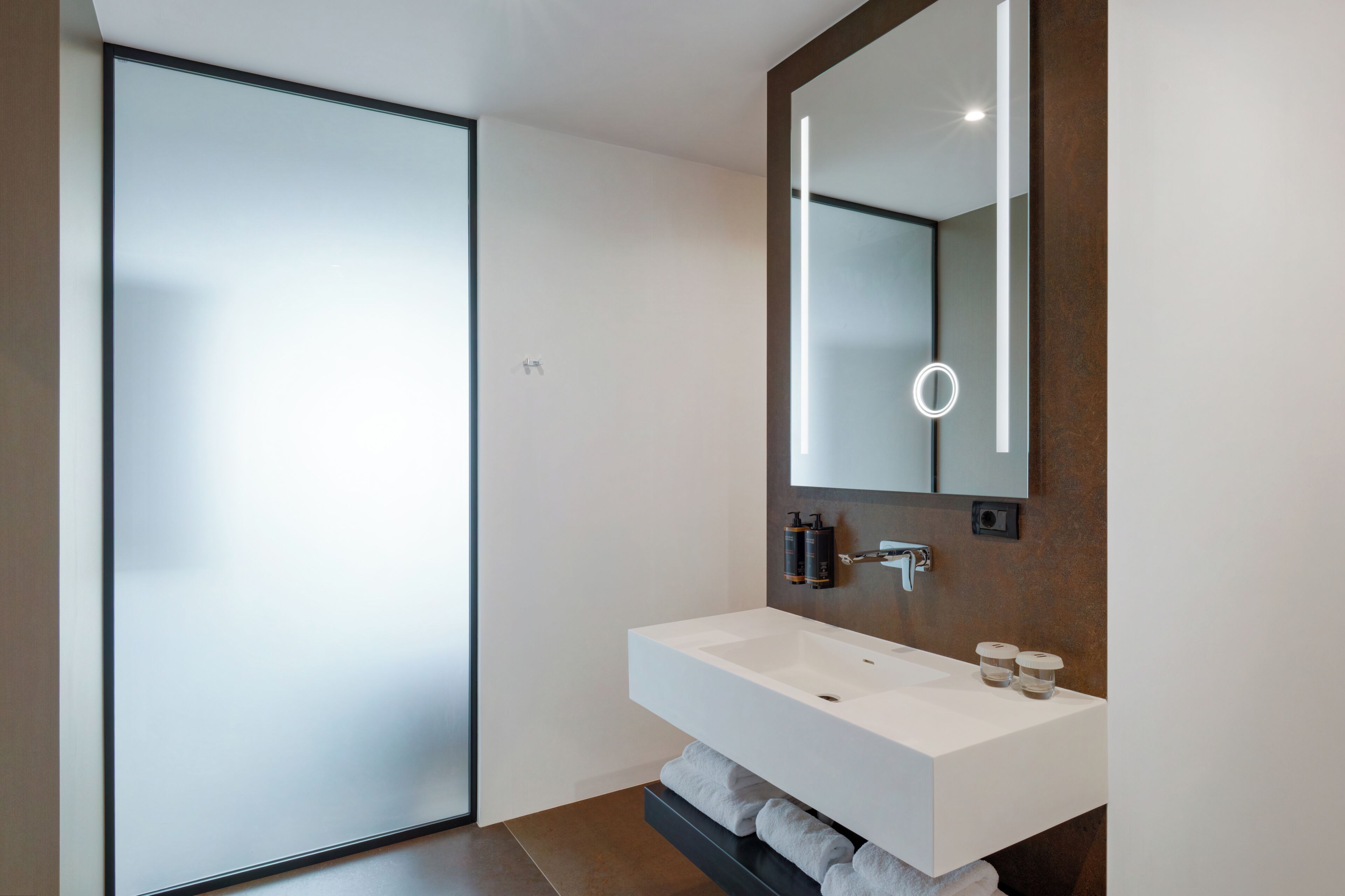 A modern bathroom with a large mirror, a white sink, and a towel rack.