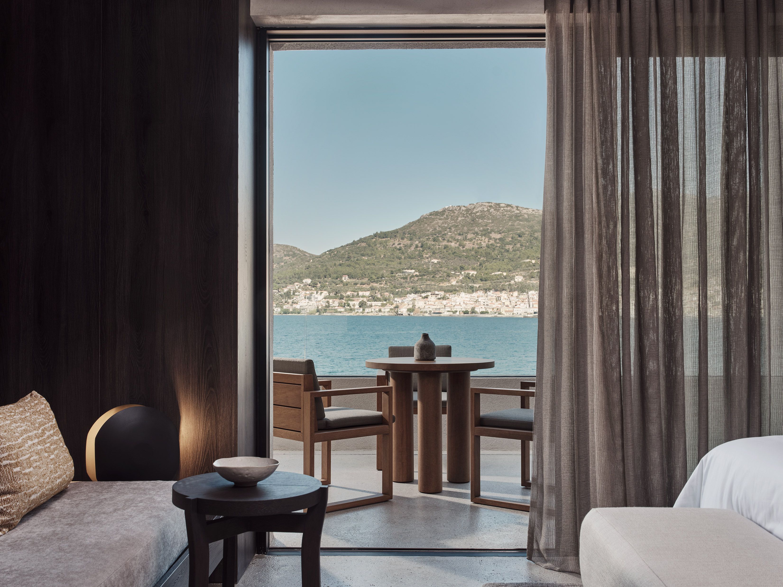A room with a view of a coastal landscape, a sofa, a table with a bowl, and a chair.