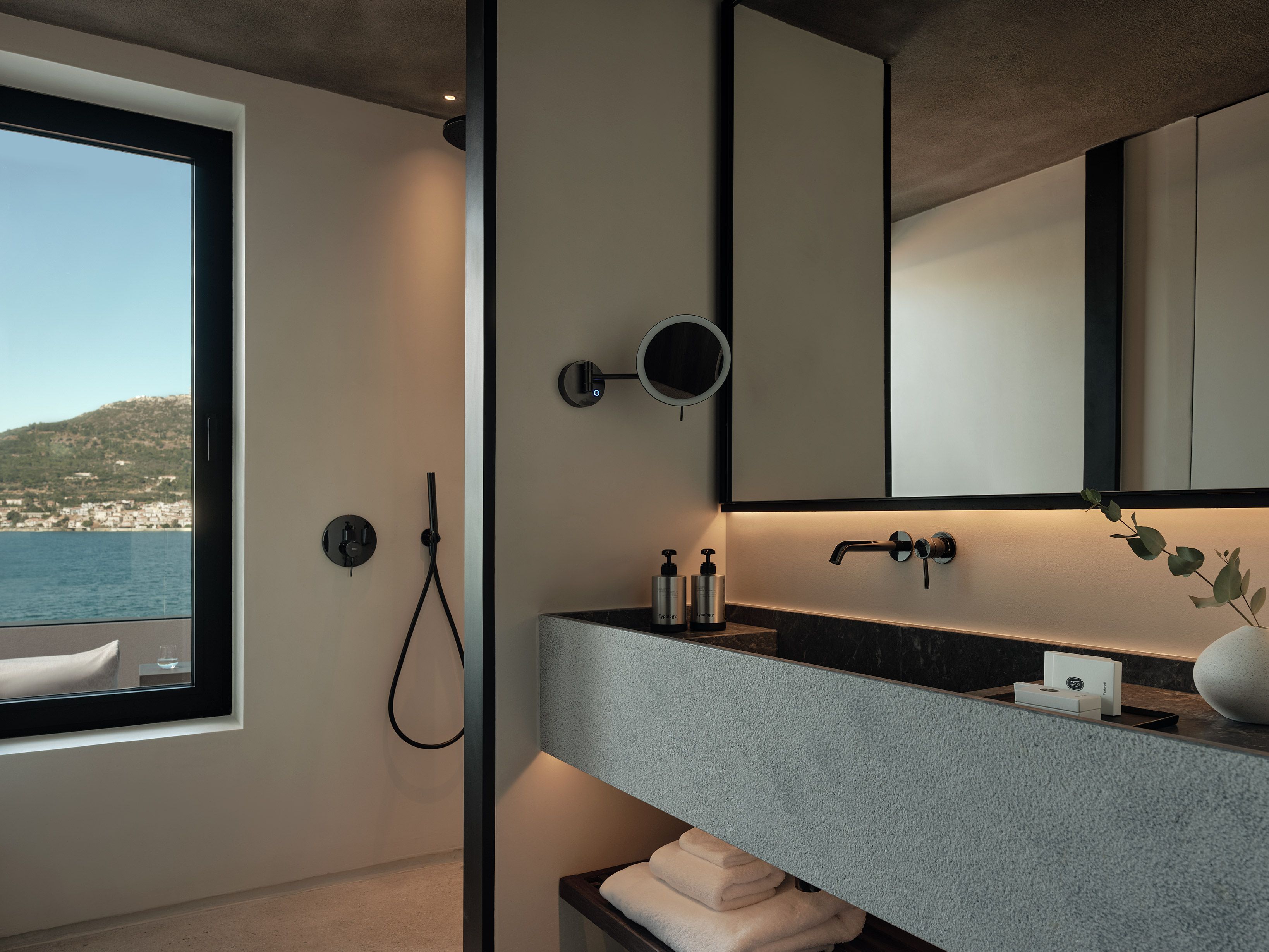 Un baño moderno con un ventanal grande, ducha, lavamanos con espejo y un perchero para toallas.