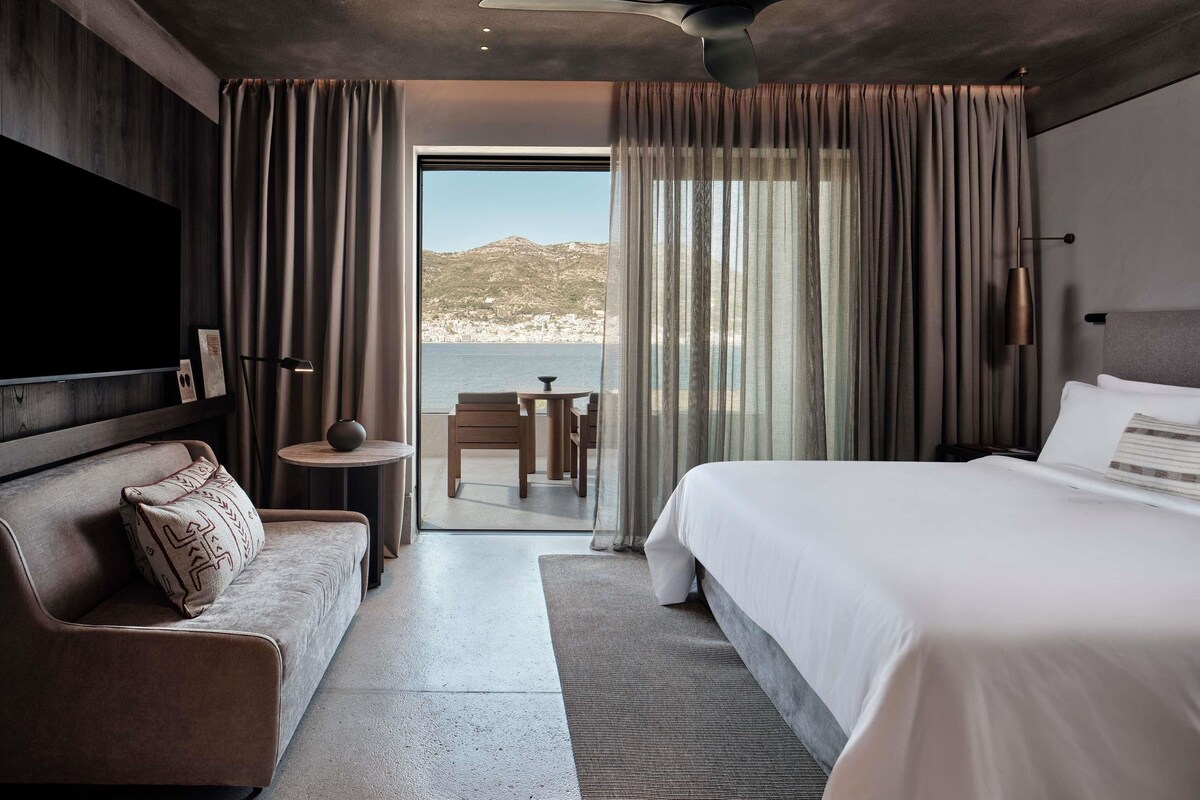 Una habitación de hotel moderna con cama, sofá, una mesita y televisor.