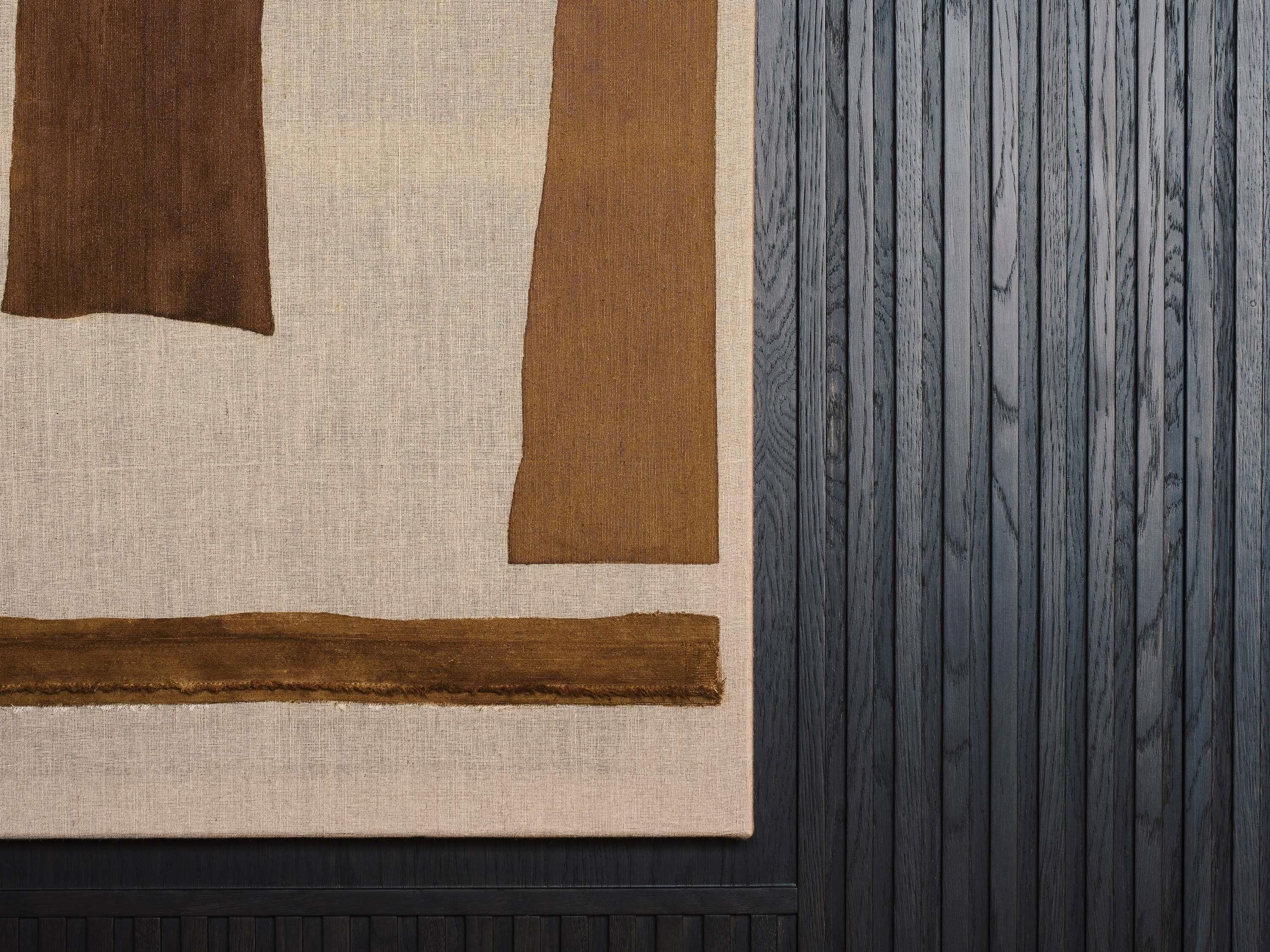 A textured wall with a dark wooden panel and a beige fabric with brown accents.