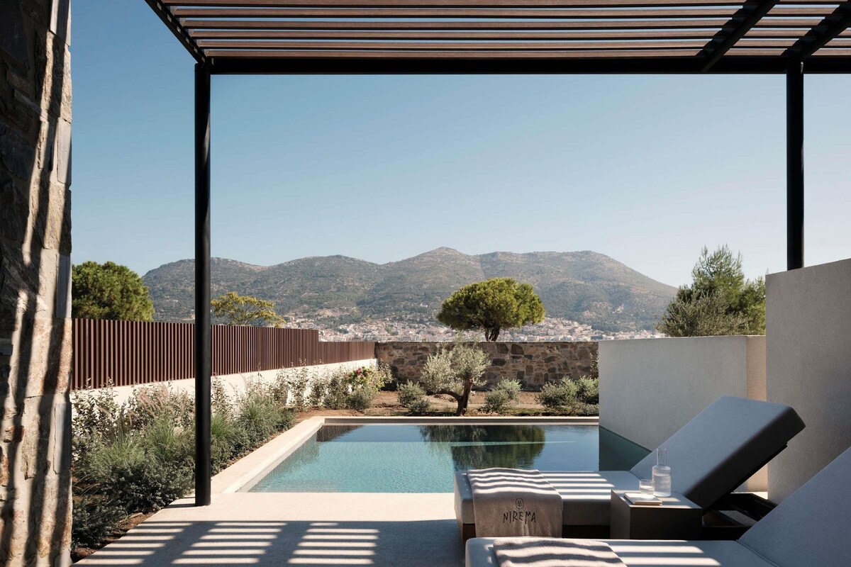 Zona junto a la piscina con sillones de descanso, pared de piedra y vistas a las montañas.
