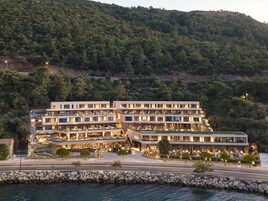 Un hotel de varios pisos con un diseño moderno, situado cerca de una masa de agua y con montañas al fondo.