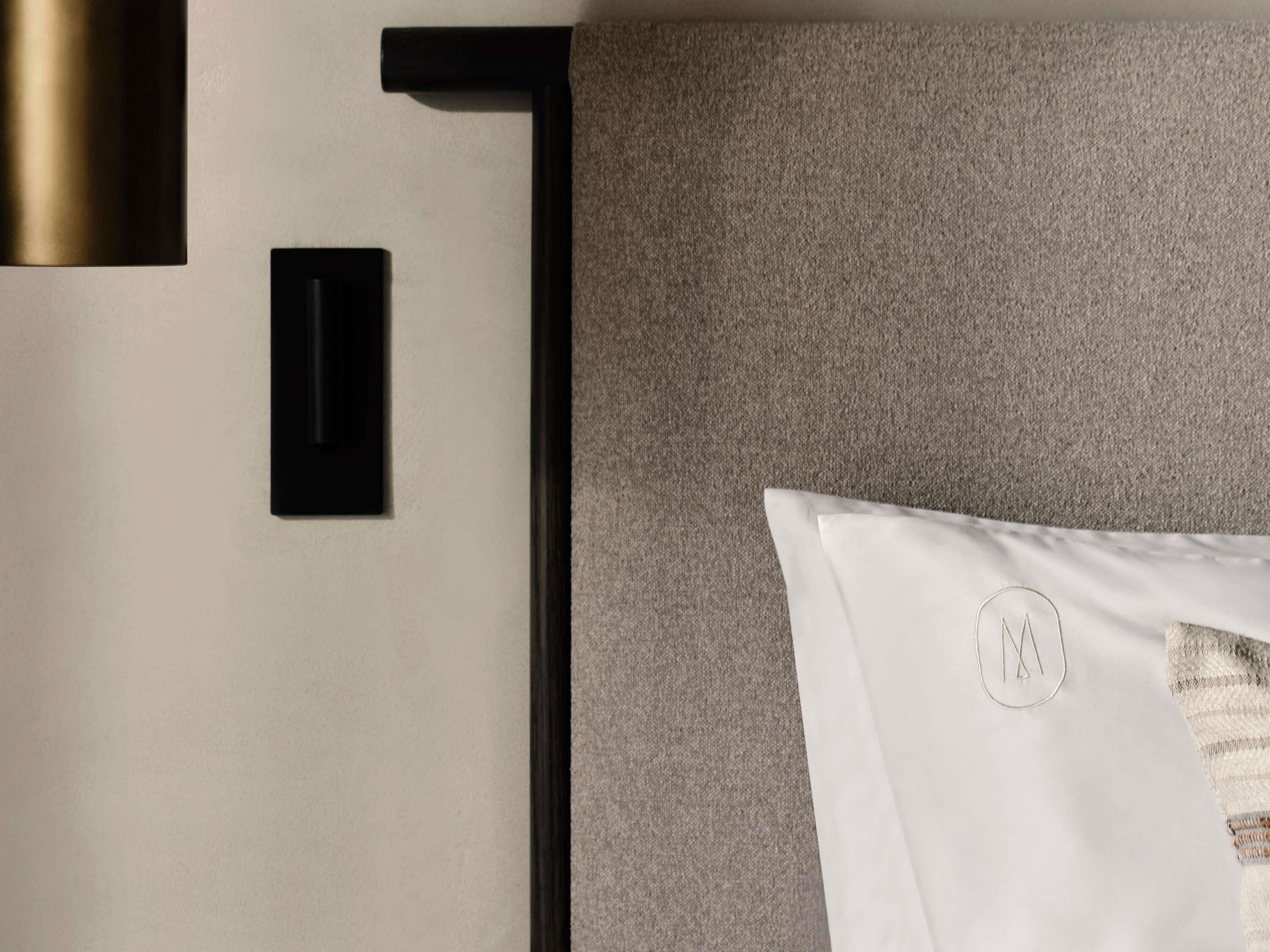 A hotel room with a bed, a wall-mounted light fixture, and a small black panel.